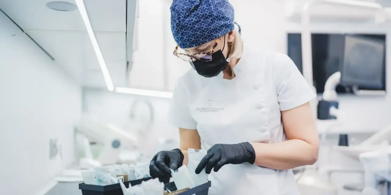 Dentystka w czepku i masce przygotowuje materiały, w tym te do zabiegów z użyciem abrazji powietrznej.