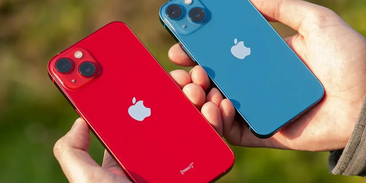 Dwie dłonie trzymają dwa telefony: czerwony i niebieski iPhone 13 mini. Aparat obu modeli jest widoczny.