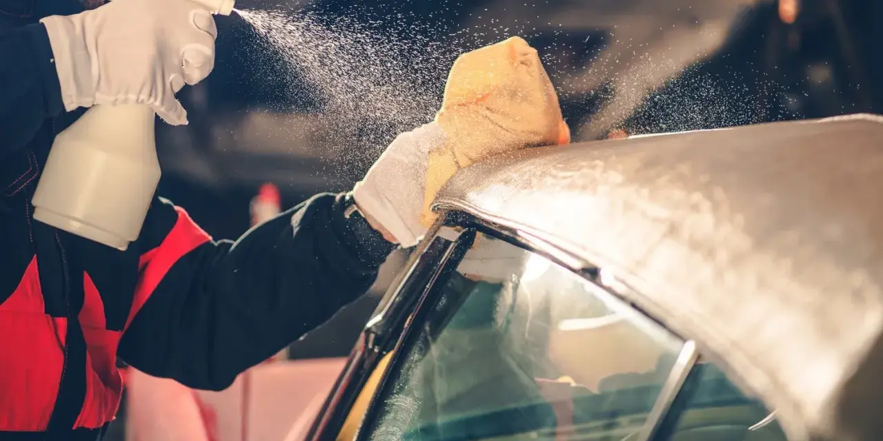 A person in gloves sprays a convertible car's fabric top with cleaning solution, then wipes it with a sponge. This is how you wash a convertible car.