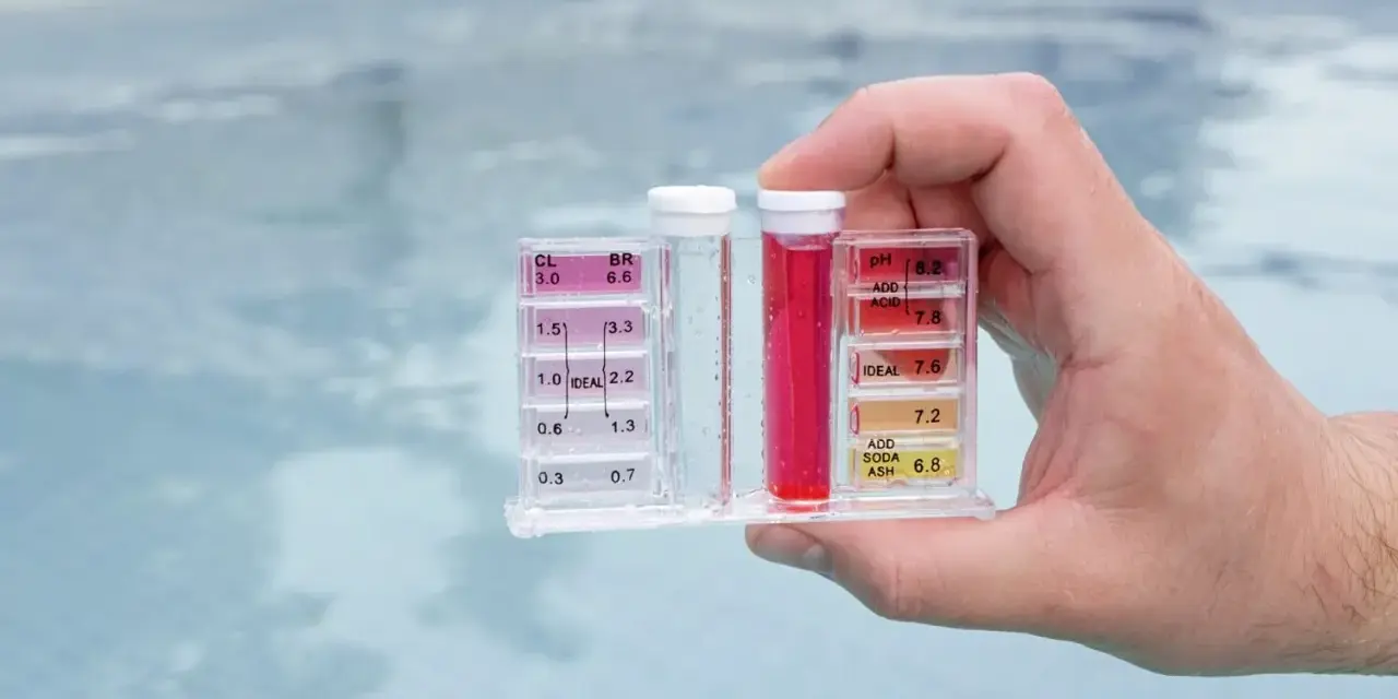 Hand holds pool water test kit. Red liquid in the pH tube indicates a high reading, suggesting acid is needed to lower pH.