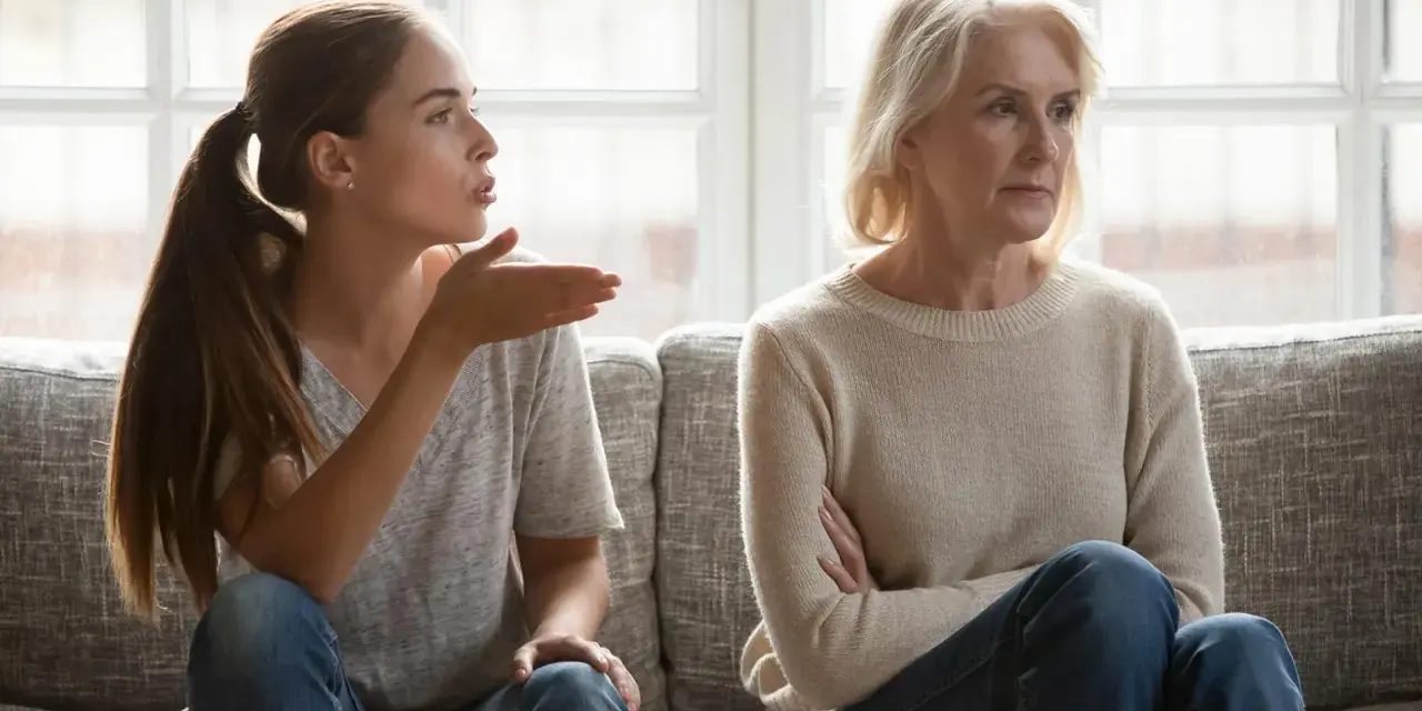 Junge Frau gestikuliert wütend, während ihre Mutter abgewandt sitzt. Es scheint, als ob meine Tochter mich hasst.