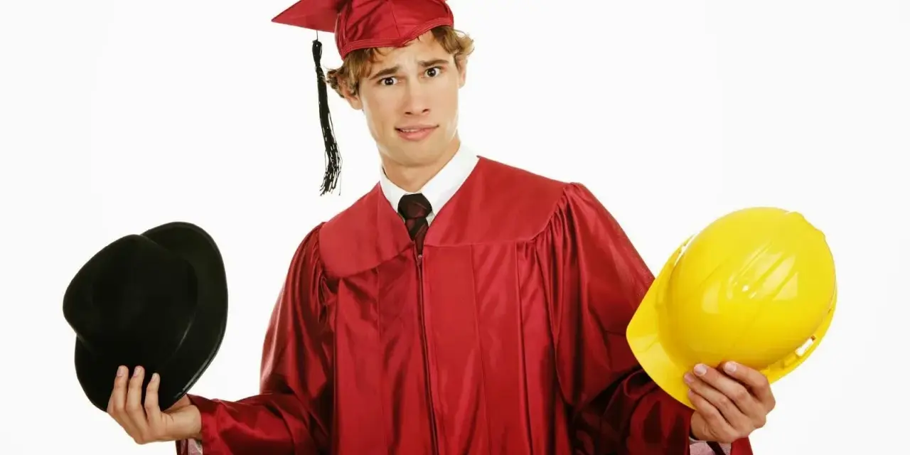 Studente universitario lavoratore con toga e cappello da laureato, tiene in mano un cappello nero e un casco giallo, indeciso sul futuro.