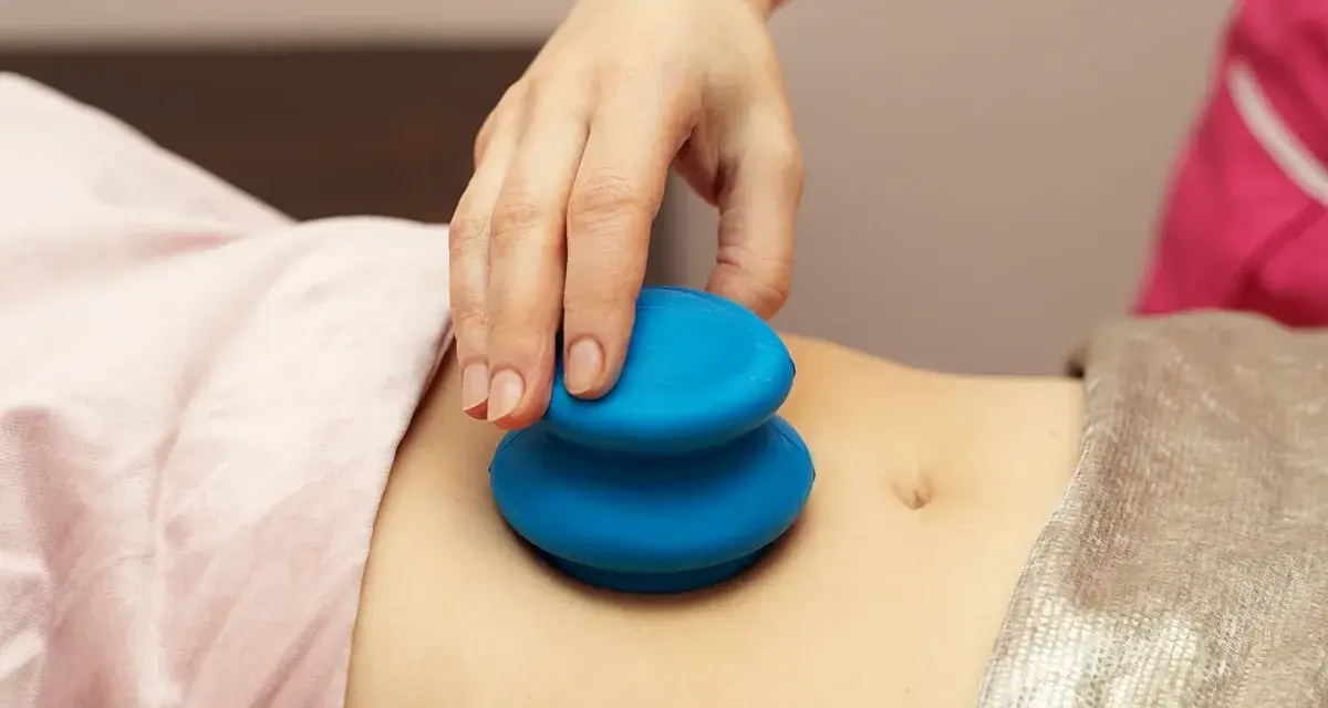 Dłoń terapeuty wykonuje masaż banką chińską na brzuchu pacjentki.
