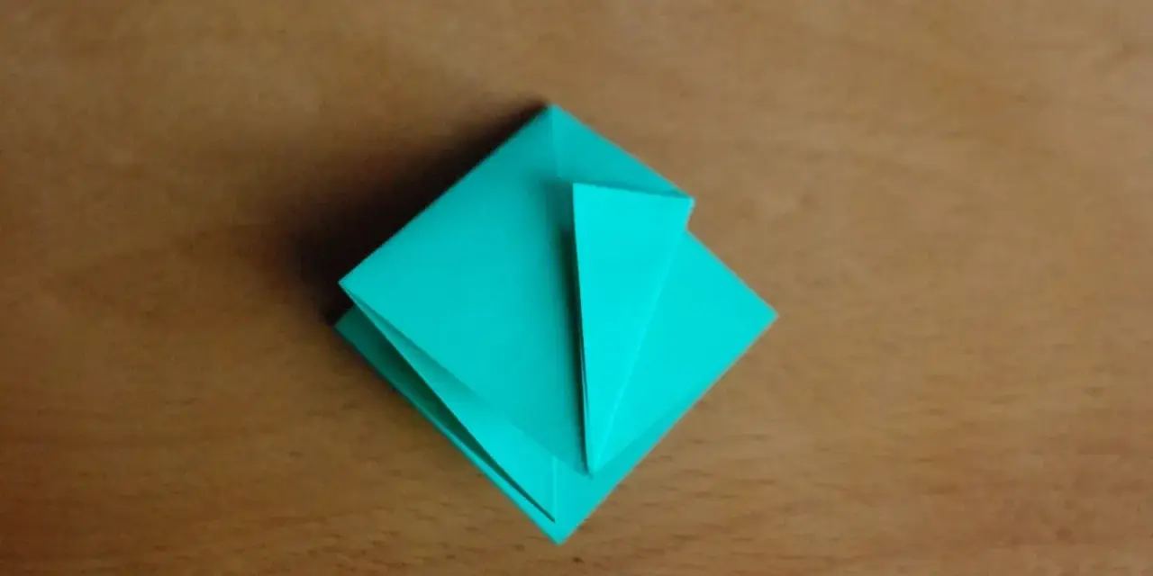 Krok 15 instrukcji, jak zrobić kwadrat z papieru. Turkusowa origami na drewnianym tle.