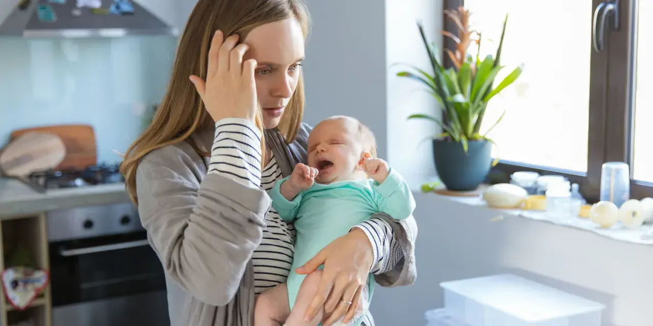 Müde Mutter hält weinendes Baby. Der **12 wochen schub** macht ihr zu schaffen. Sie hält sich die Stirn.