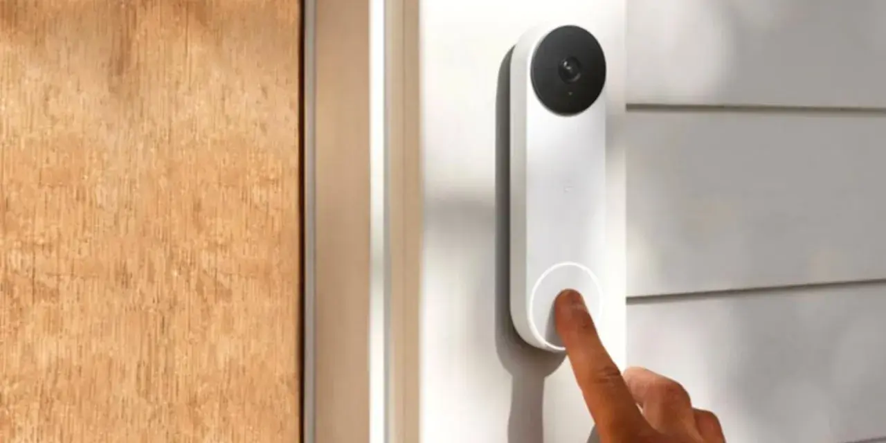 Un dedo presiona qué es el timbre inteligente, un dispositivo blanco con cámara negra, junto a una puerta de madera.