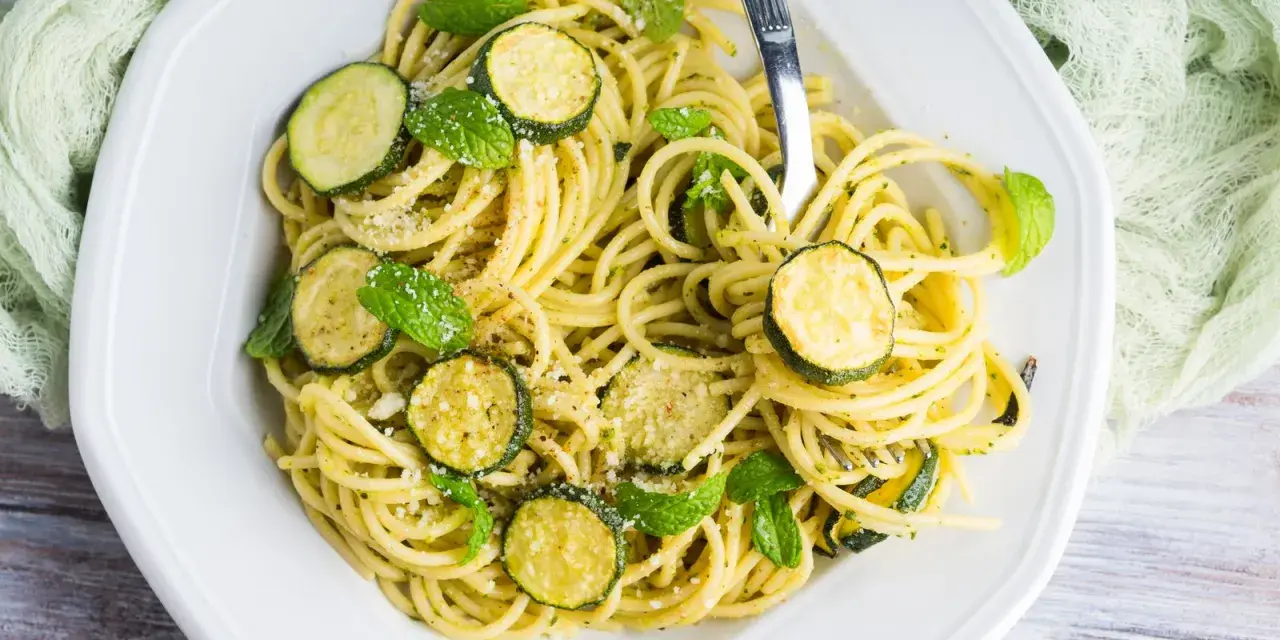 Spaghetti con zucchine cremosa, guarniti con foglie di menta fresca e parmigiano grattugiato. Un piatto leggero e gustoso.