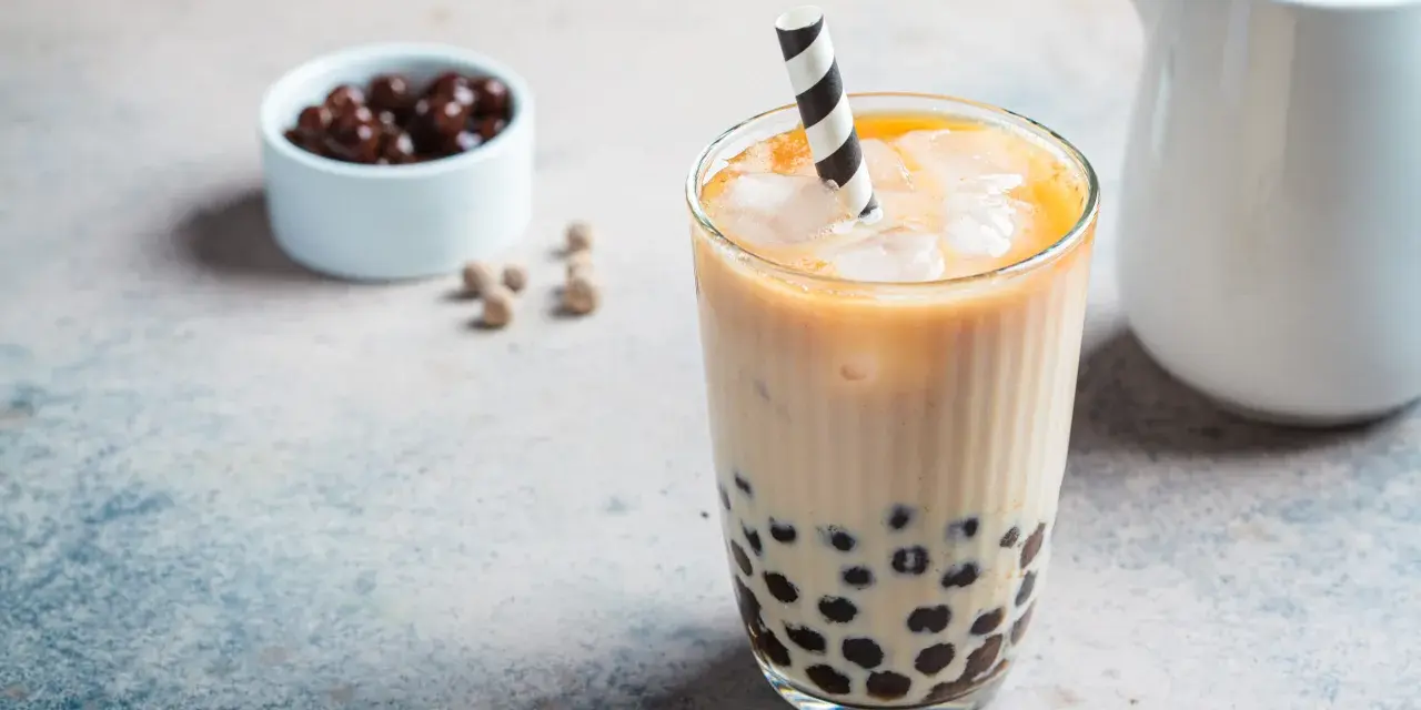 Erfrischendes Bubble Eis mit Tapiokaperlen und Eiswürfeln in einem Glas, daneben eine Schale mit dunklen Perlen.
