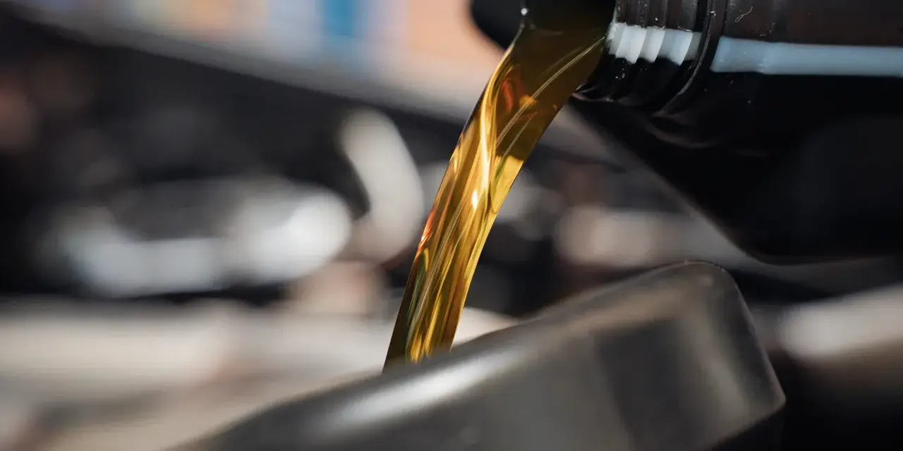 Goldfarbenes Motoröl fließt aus einem schwarzen Behälter in einen dunklen Trichter.