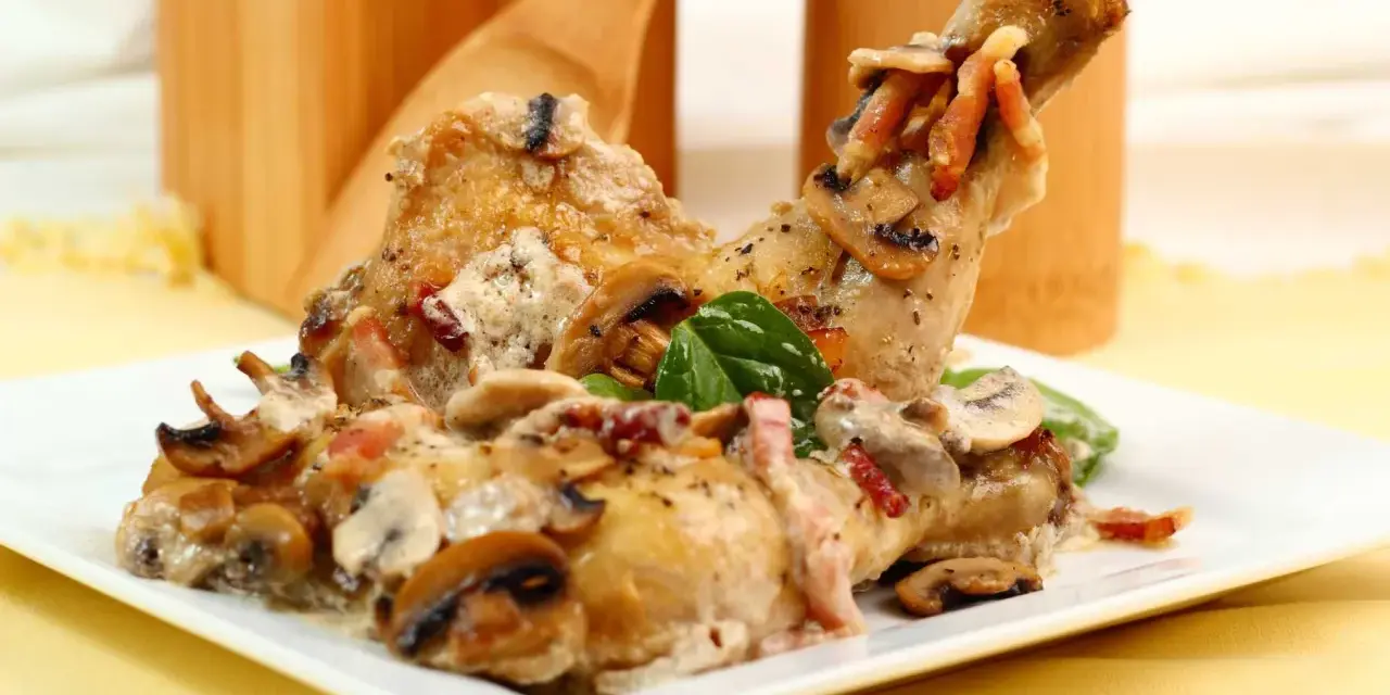 Delicioso pollo con champiñones y tocino en una cremosa salsa, servido en un plato blanco.