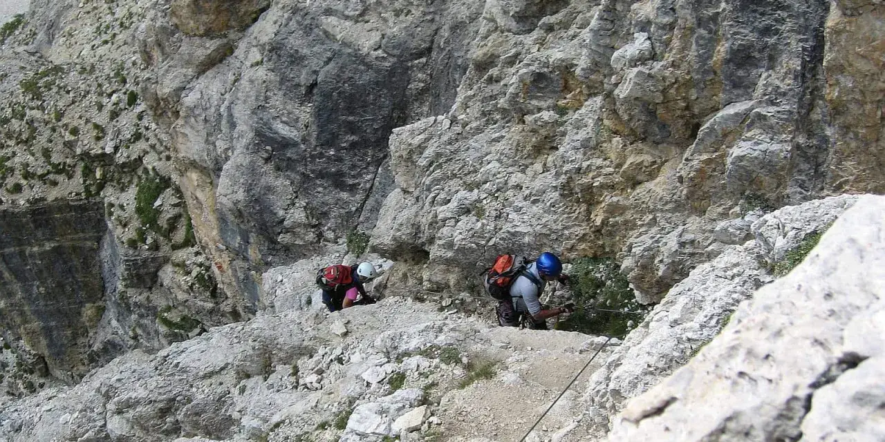 Dwóch turystów pokonuje via ferraty w Dolomitach, wspierając się na stalowej linie.