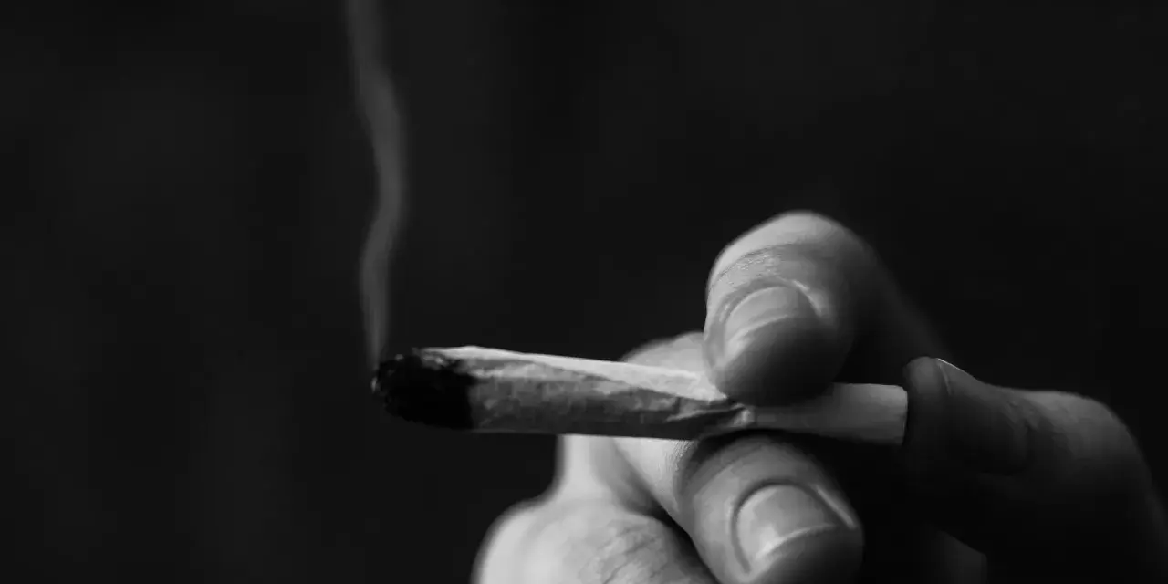 A hand holds a lit joint, smoke curling upwards. This image prompts reflection on whether Christians can smoke weed.