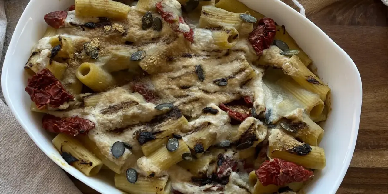 Piatto di pasta con carciofi alla siciliana, pomodori secchi e semi di zucca, gratinata al forno.