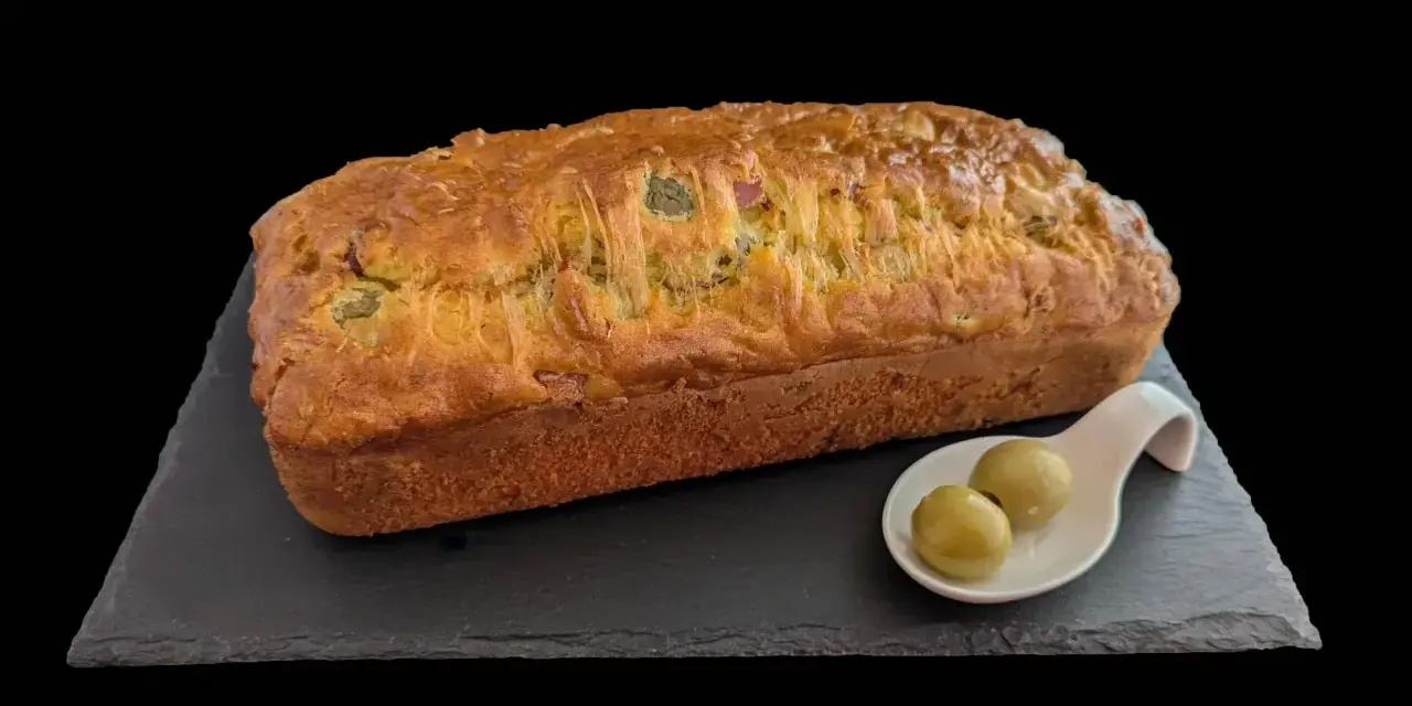 Un délicieux cake jambon olive, doré et moelleux, servi avec deux olives vertes sur une cuillère.