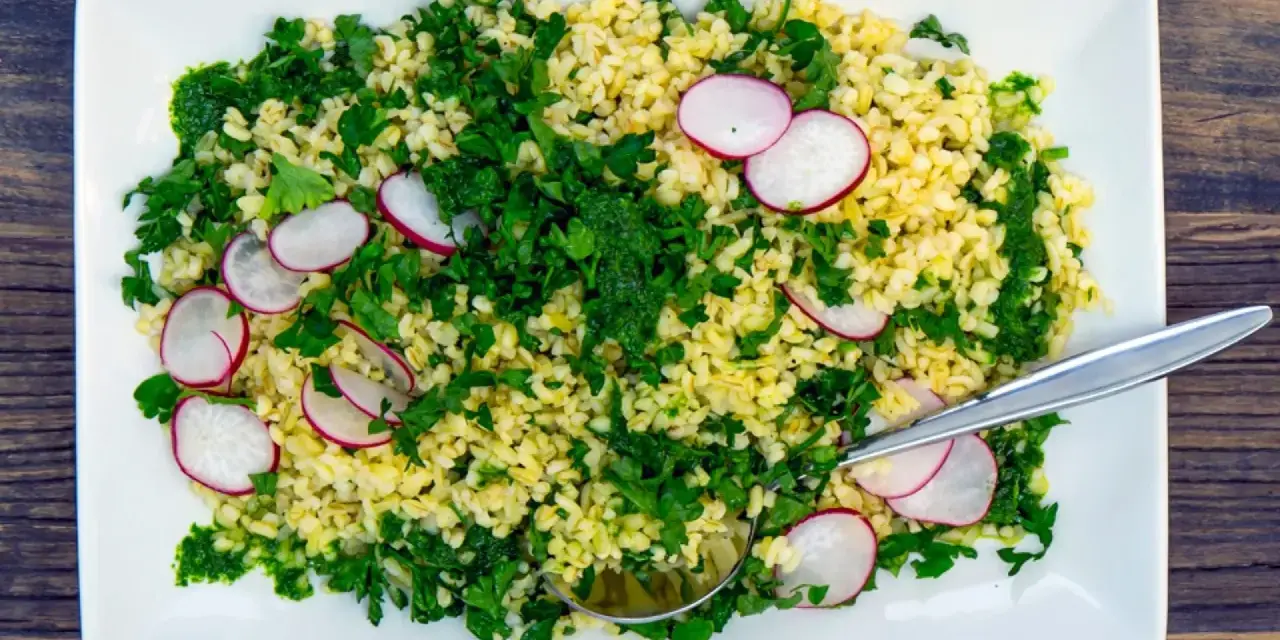 En fräsch bulgursallad med rädisor och färska örter, serverad på en vit tallrik med en sked.
