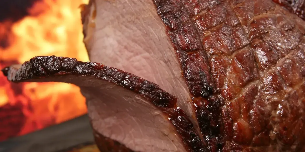 Un enchaud de porc juteux, rôti à la perfection, avec une croûte caramélisée et des flammes dans l'arrière-plan.