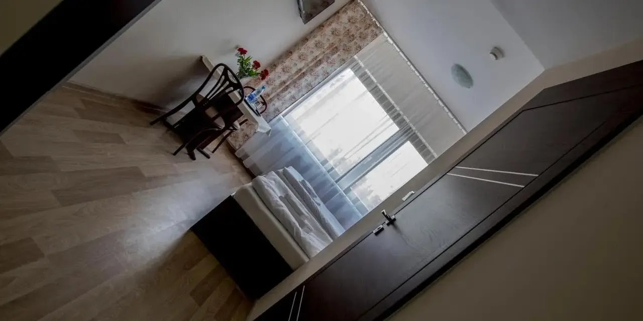 Pokój w hotelu i restauracji Crystal: łóżko, stolik z krzesłami i kwiatami, okno z zasłonami.