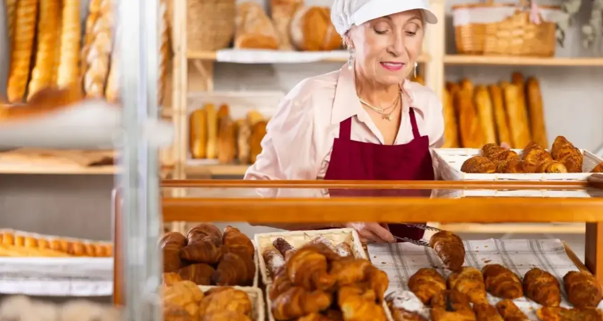 Starsza pani piekarz z uśmiechem układa świeże croissanty. To ulga dla pracujących seniorów, którzy wciąż mają pasję.