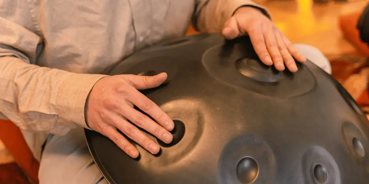 Dłonie grają na instrumencie typu hang drum, tworząc kojące dźwięki.