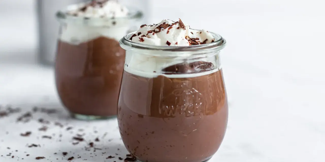 Zwei Gläser mit cremigem omas schokoladenpudding, gekrönt mit Schlagsahne und Schokostreuseln.