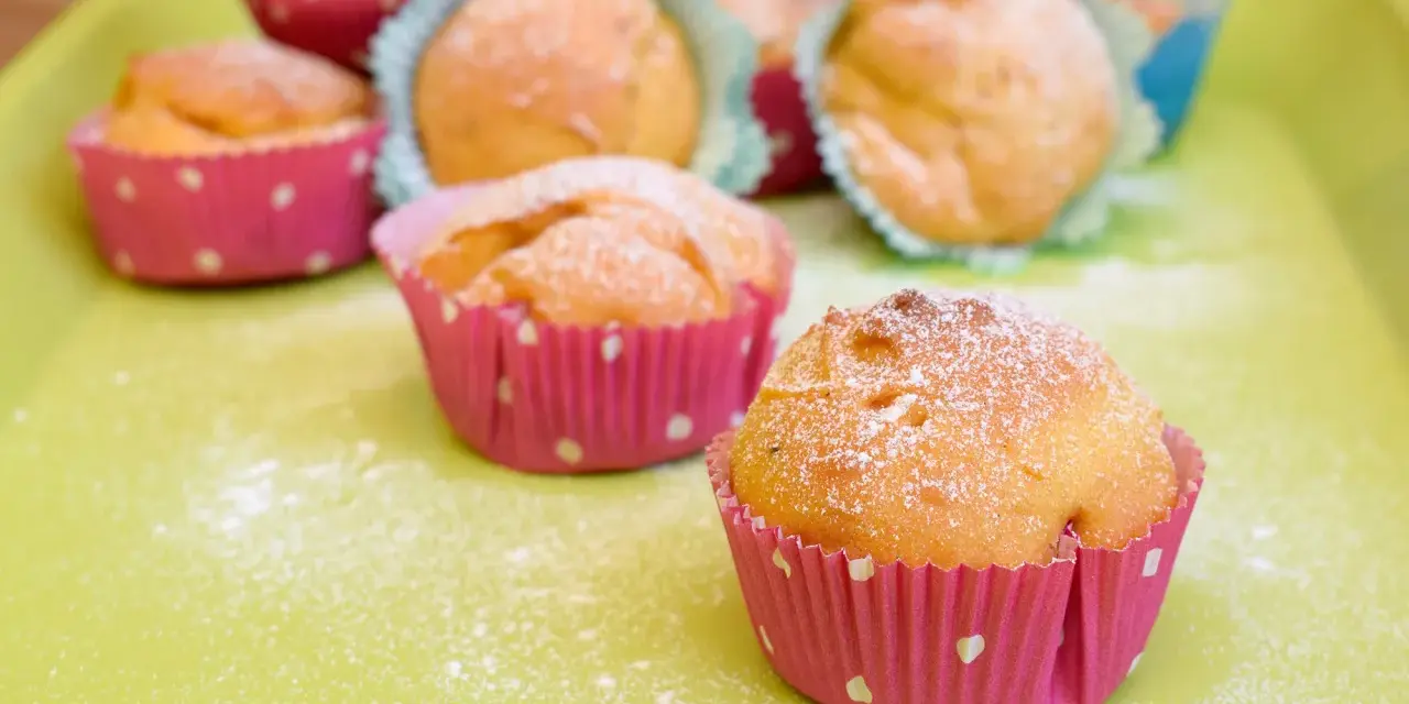 Leckere Muffins ohne Ei, bestäubt mit Puderzucker, in bunten Papierförmchen auf einer hellgrünen Platte.