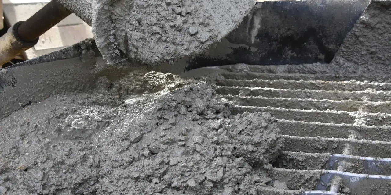 Świeży beton z kruszywem, idealny jako jaki beton pod obrzeża, wylewany z maszyny na ruszt.