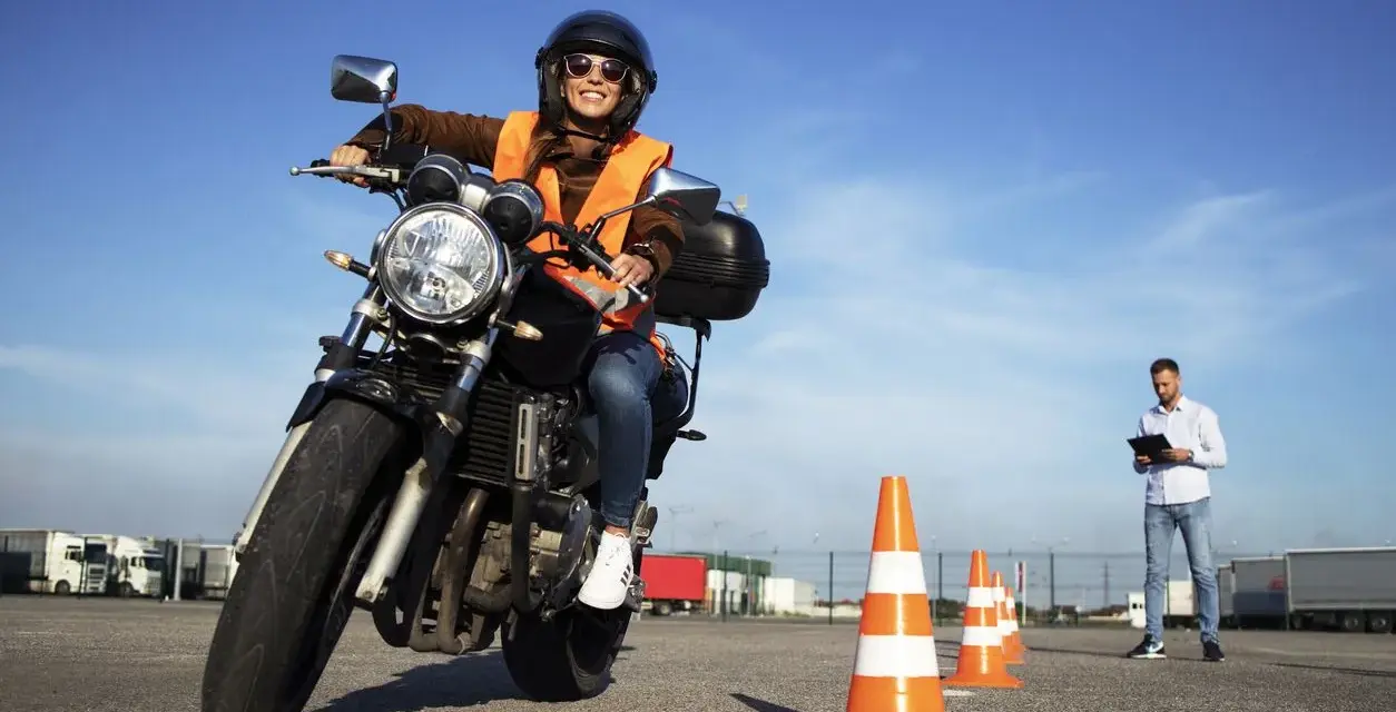 Joven sonriente en moto, lista para obtener el carnet de moto 49cc. Instructor observa en el fondo.