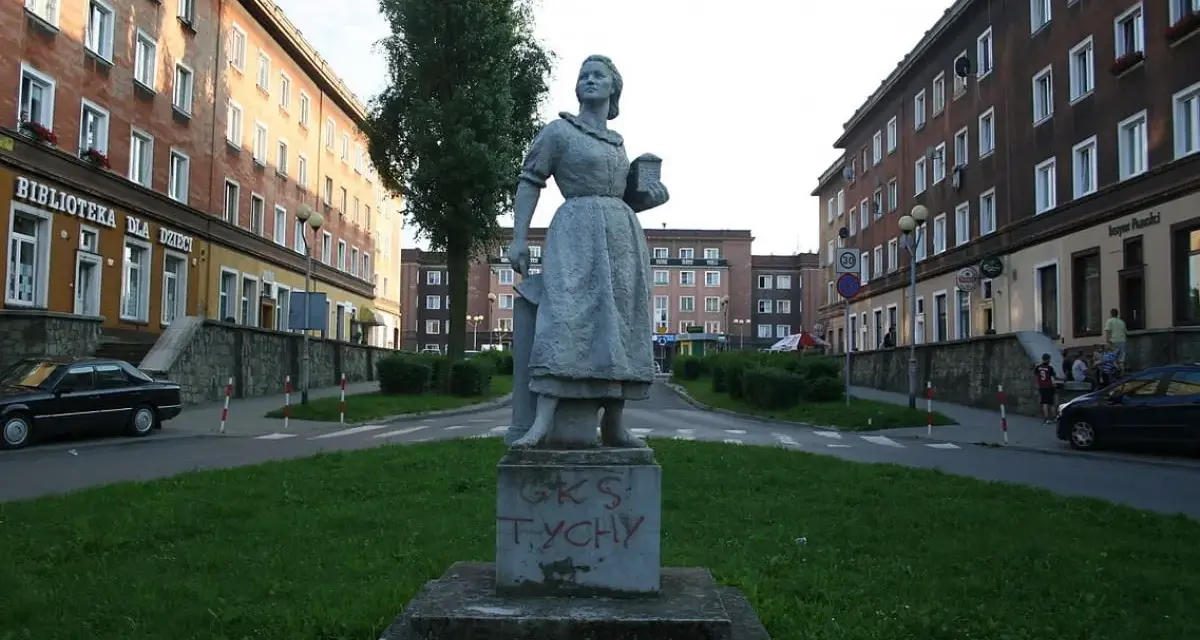 Pomnik w stylu socrealizmu na tle bloków mieszkalnych.