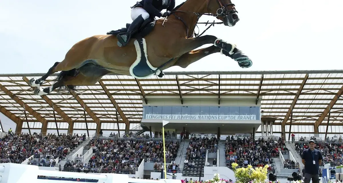 Un cavalier et son cheval s'envolent au-dessus d'une rivière lors d'un CSI Equitation. Le public applaudit dans les gradins.