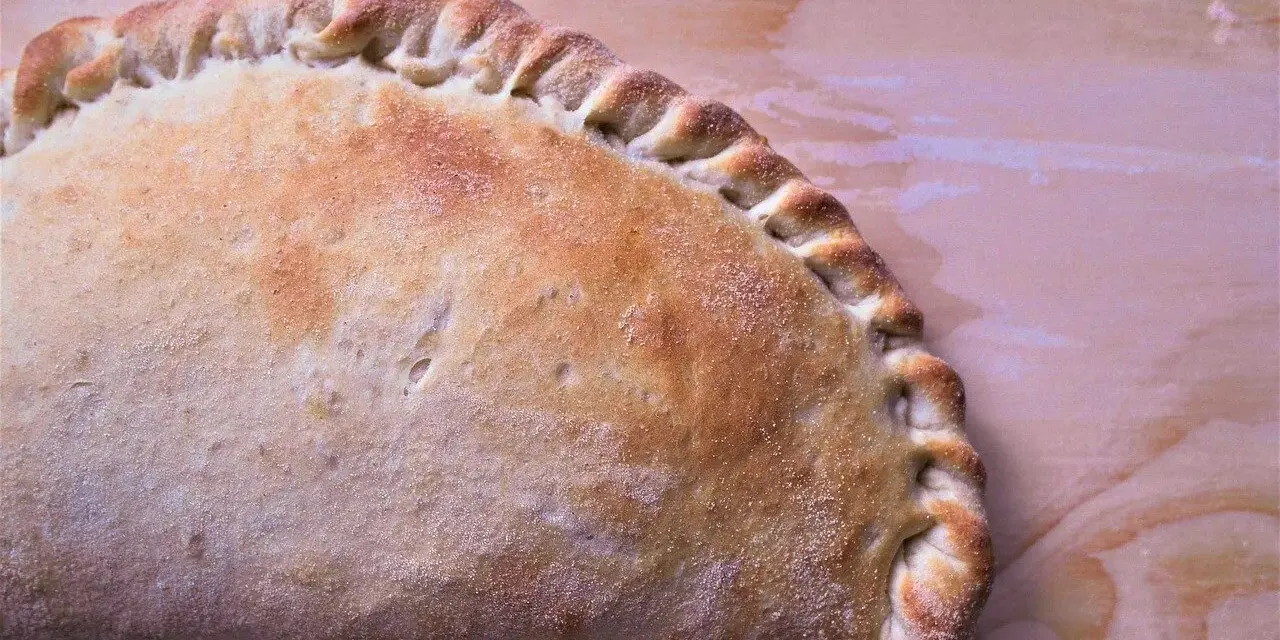 Złocisty calzone, pieczony na drewnianym tle, z charakterystycznym, zaplecionym brzegiem. Idealny na szybki posiłek.