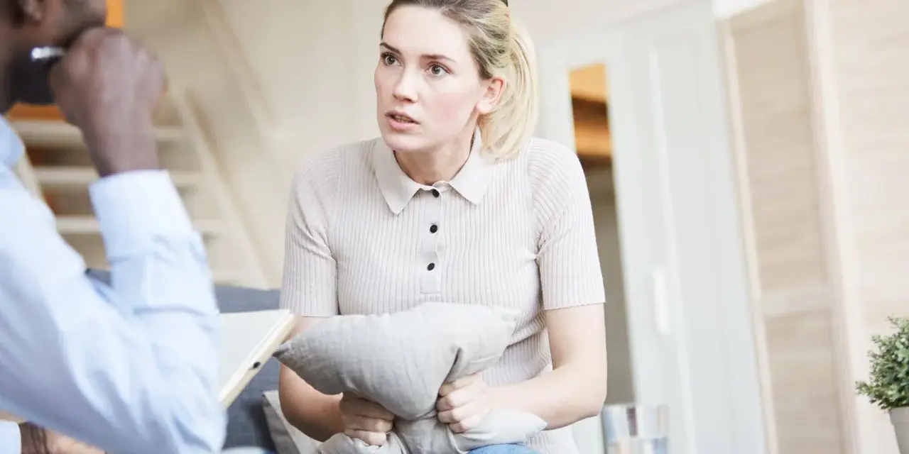 Kobieta w trakcie sesji u psychiatry, ściska poduszkę, szukając ukojenia.