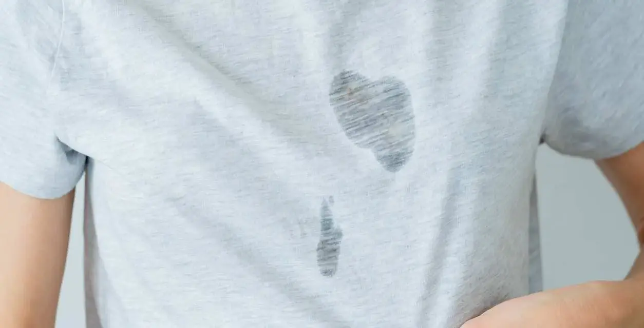 Gros plan sur une tache d'huile sur un vêtement gris clair. La tache est sombre et semble avoir pénétré le tissu.