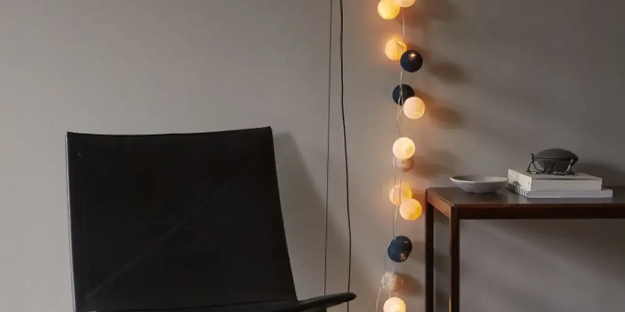 En svart läderfåtölj står bredvid ett bord med böcker och en skål. En ljusslinga med runda ljus ger en mysig inredning med ljusslingor.