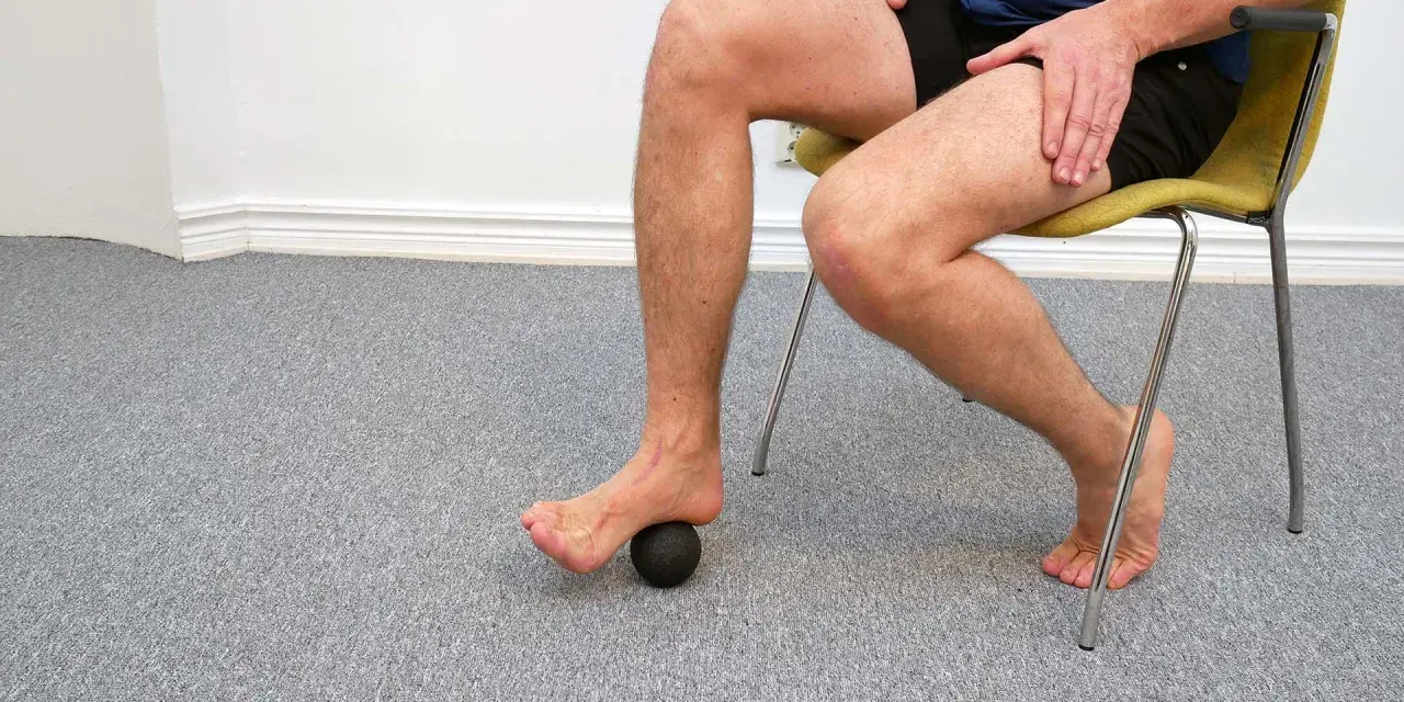 Man sitter på en stol och använder en liten boll för att rulla under foten.