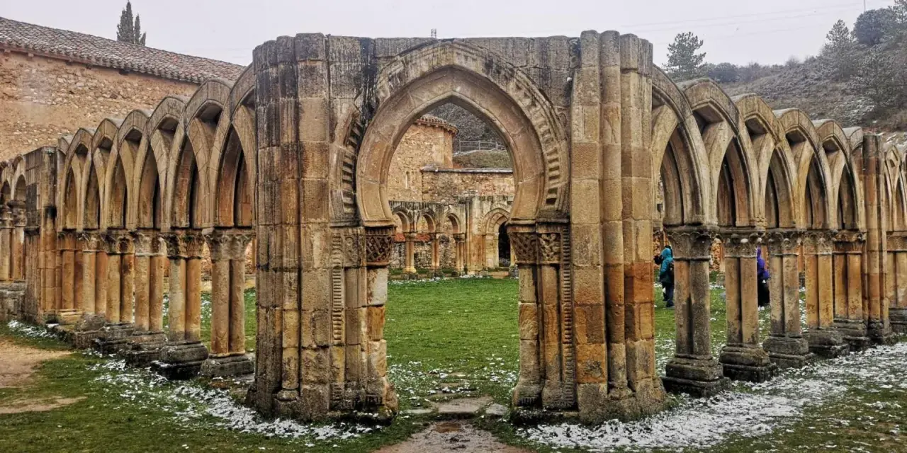 Ruinas de un claustro con arcos de piedra, evocando el nacimiento del Duero. Nieve ligera cubre el césped.