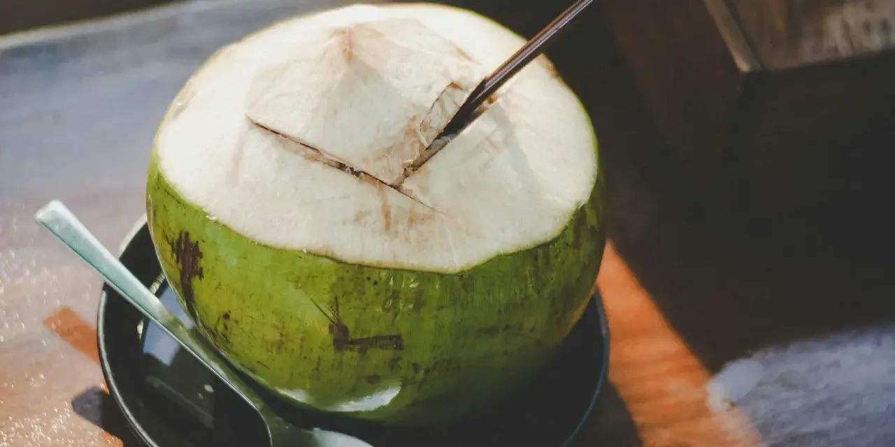 Une noix de coco verte ouverte avec une paille, prête à déguster. Découvrez les nombreux bienfaits de l'eau de coco pour une hydratation naturelle.