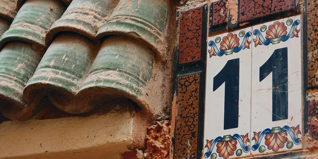 Numerologiczna 11 mężczyzna, jak liczba 11 na ozdobnej tabliczce obok zielonych dachówek, symbolizuje intuicję i duchowość.