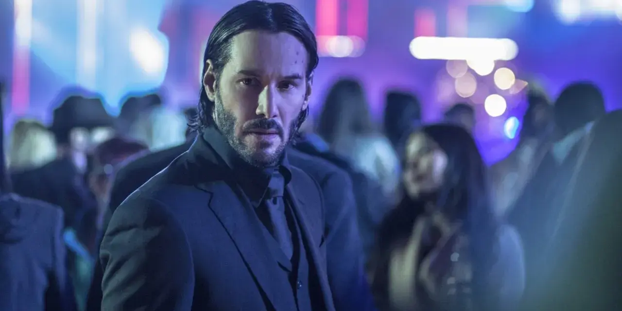 Keanu Reeves w garniturze, w tle rozmyte światła i tłum. Ikona kina akcji, znana z filmów takich jak John Wick.