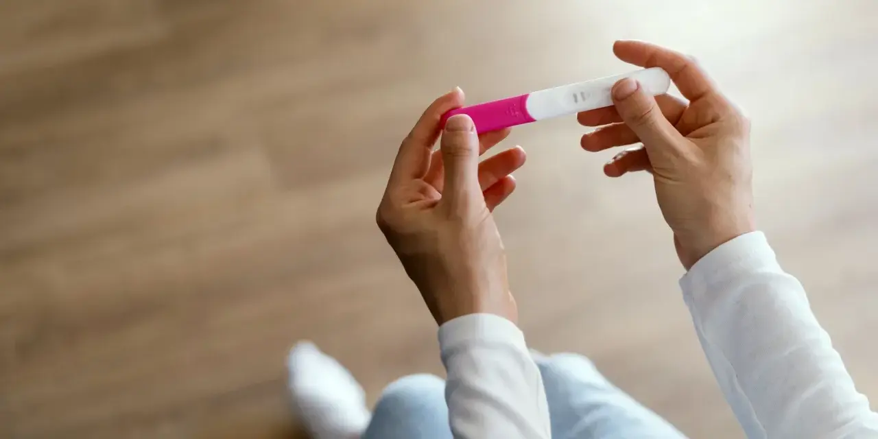 Dłonie trzymające test ciążowy z dwoma kreskami.