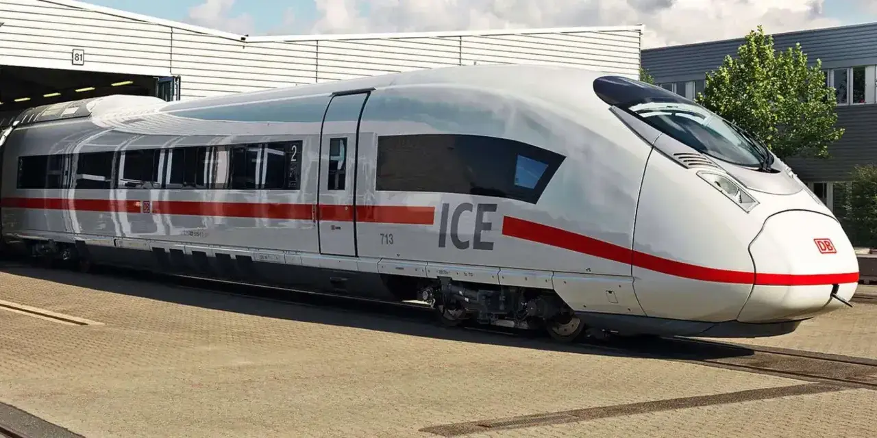 Biały pociąg ICE 5 z czerwonym pasem stoi na torach przed budynkiem.