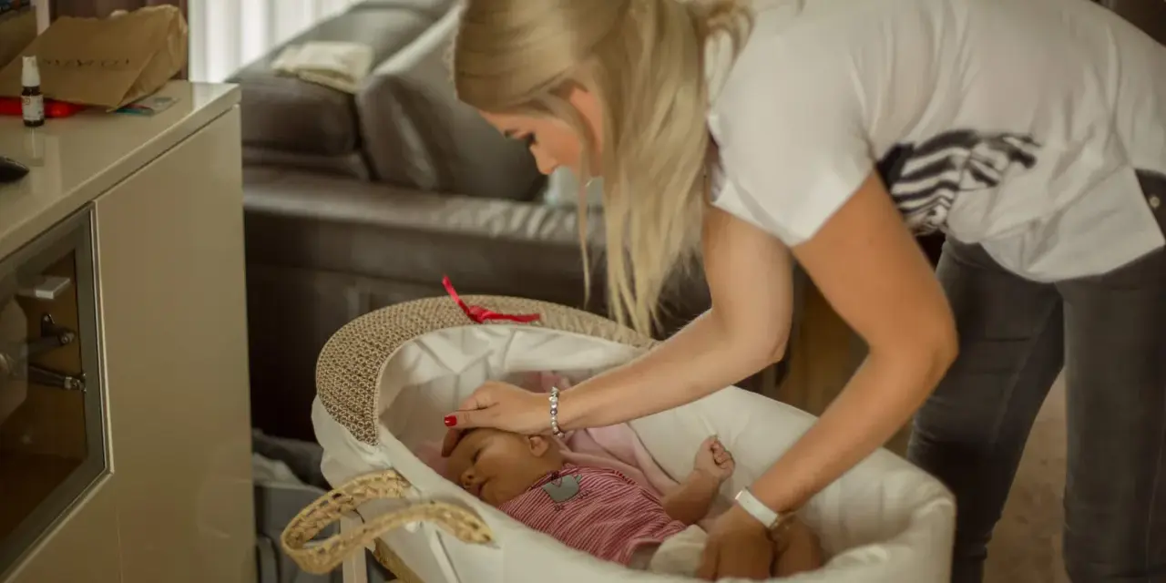Mama delikatnie kładzie śpiące dziecko do kosza. To początek nauki samodzielnego zasypiania bez płaczu.