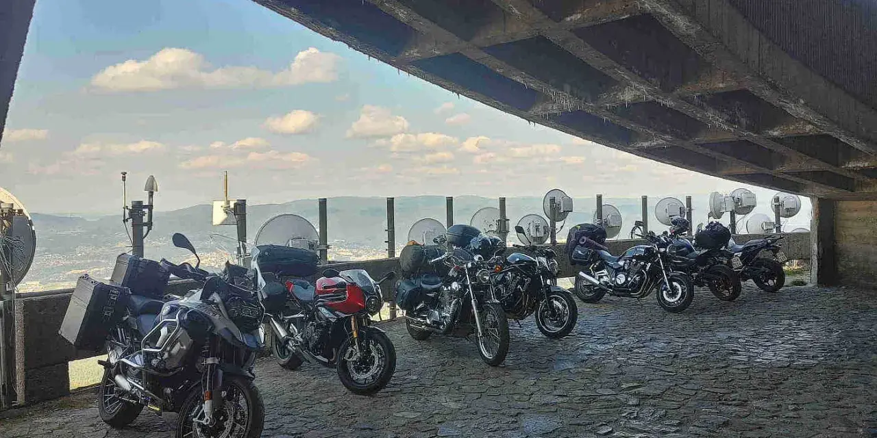 Motocykle pod betonowym zadaszeniem, z widokiem na krajobraz przypominający szwajcarskie Czechy.