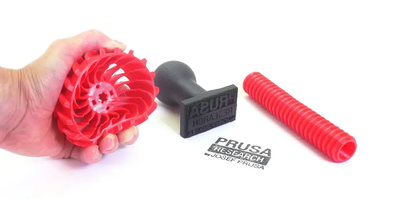Czerwony, elastyczny filament w kształcie wirnika, stempel z logo Prusa Research i czerwona rurka.