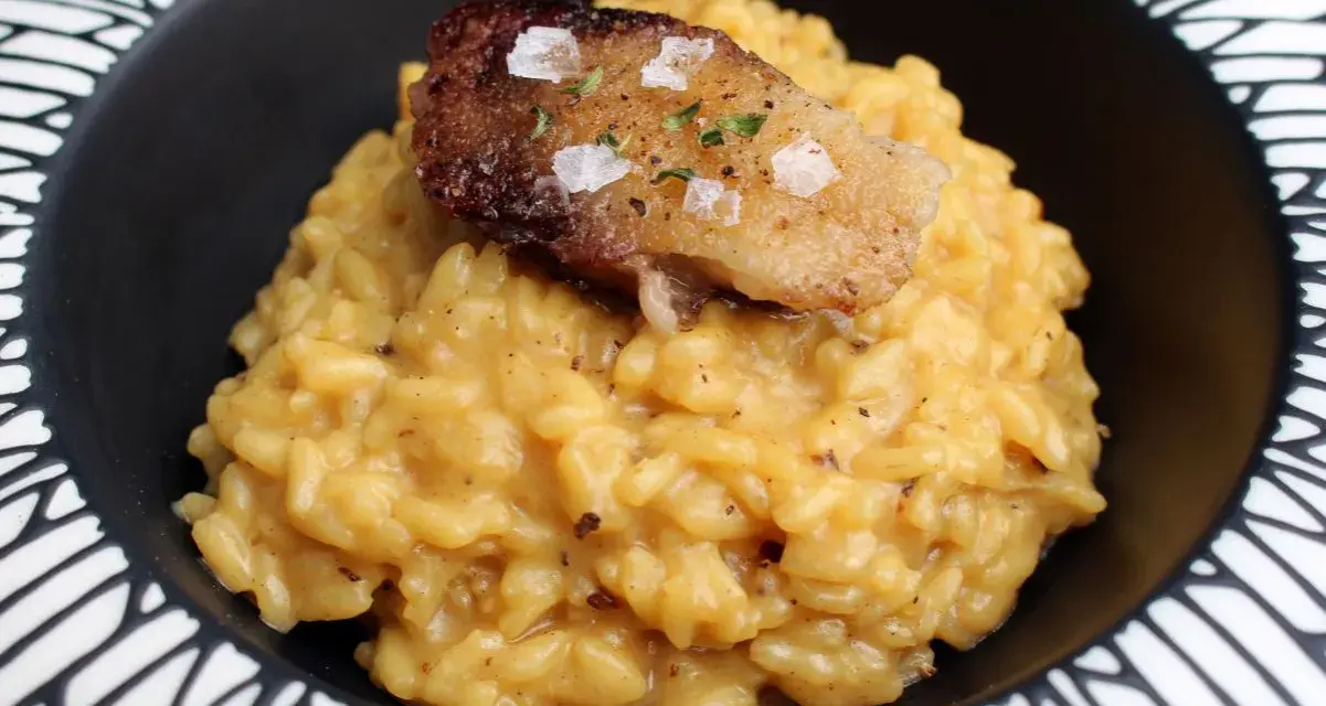 Cremoso risotto a la milanesa, coronado con un trozo crujiente y salpicado de sal marina y hierbas.