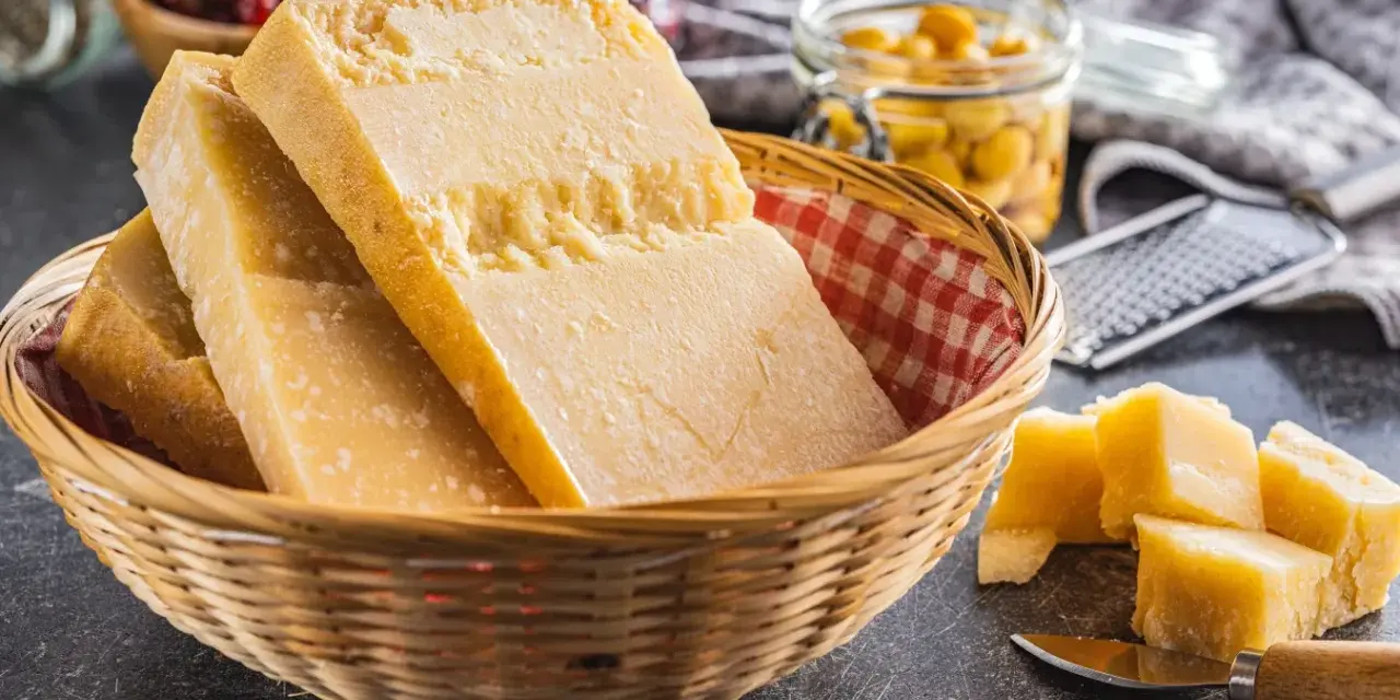 Kosz z kawałkami żółtych, twardych serów podpuszczkowych, obok pokrojone w kostkę sery i tarkka.