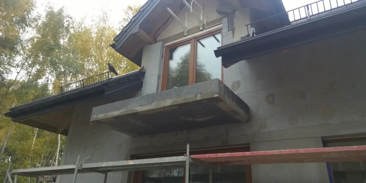 Budowa domu w toku, trwa ocieplenie ścian. Widać rusztowania i niedokończony balkon.