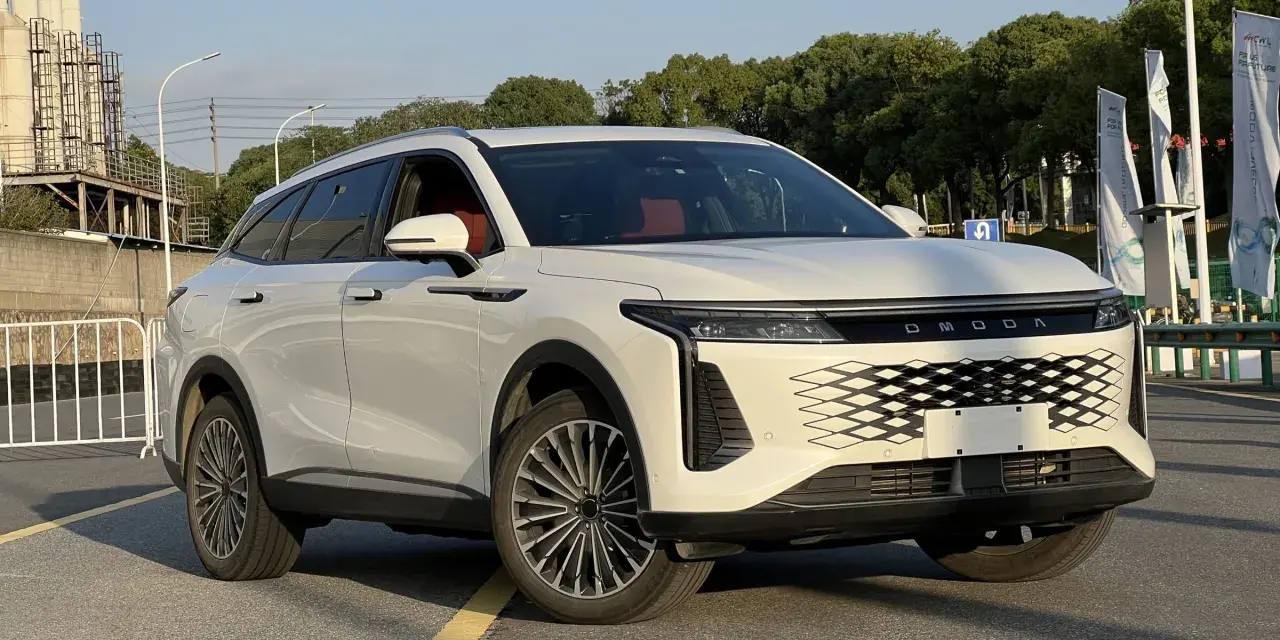Biały OMODA 9 Super Hybrid z czerwonym wnętrzem na tle przemysłowego krajobrazu.