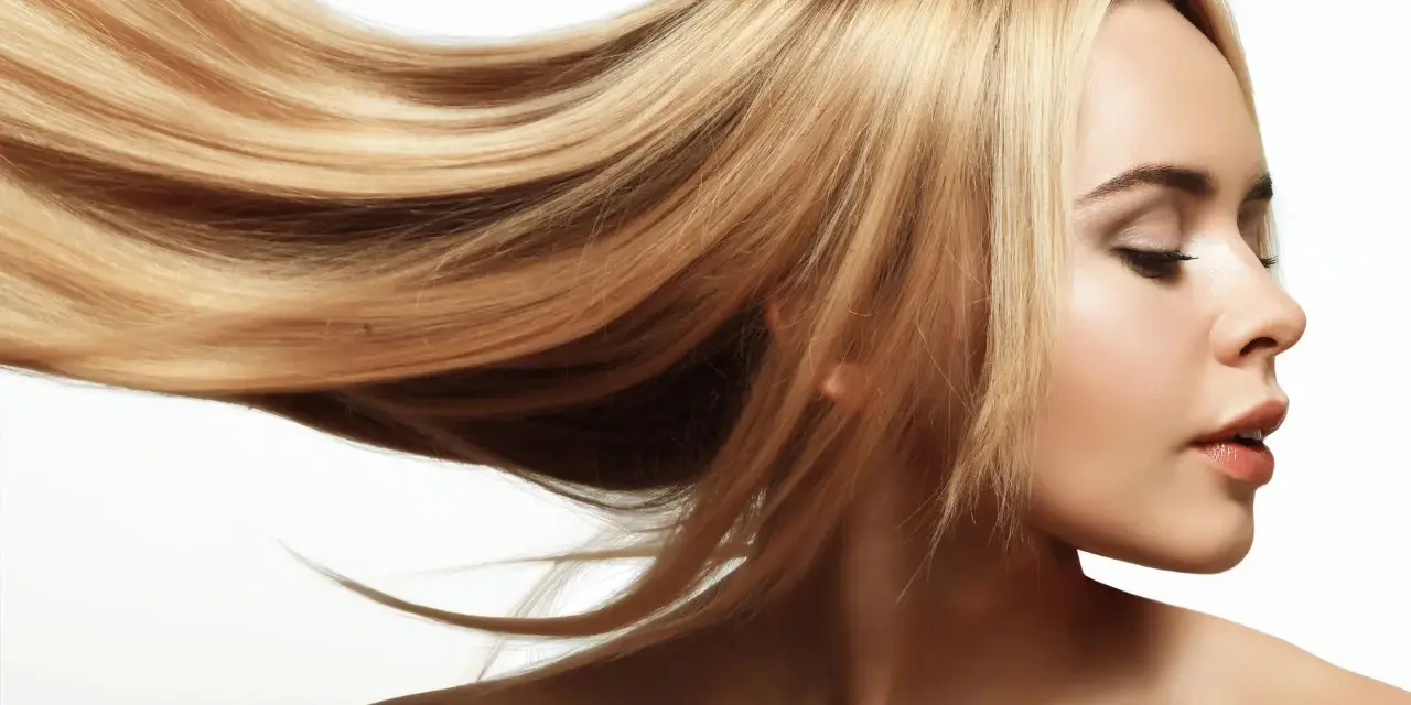 Blond włosy falujące na wietrze, lśniące jak po płukance octowej. Delikatny profil kobiety z zamkniętymi oczami.