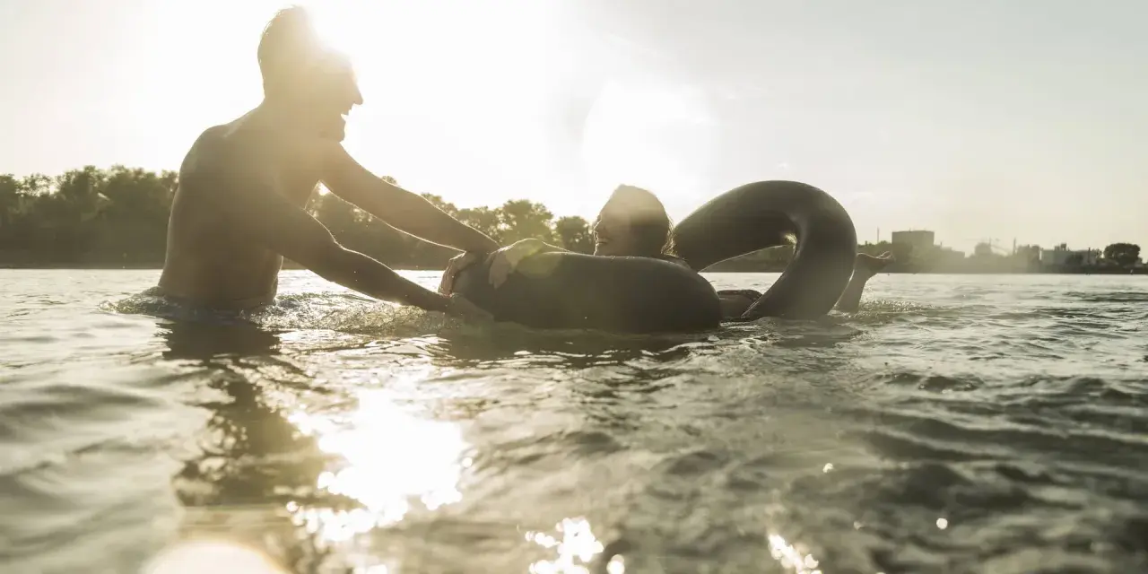 Ein Mann hilft einer Frau mit einem Schwimmring im Wasser. Ein sonniger Tag am Badesee Braunschweig.