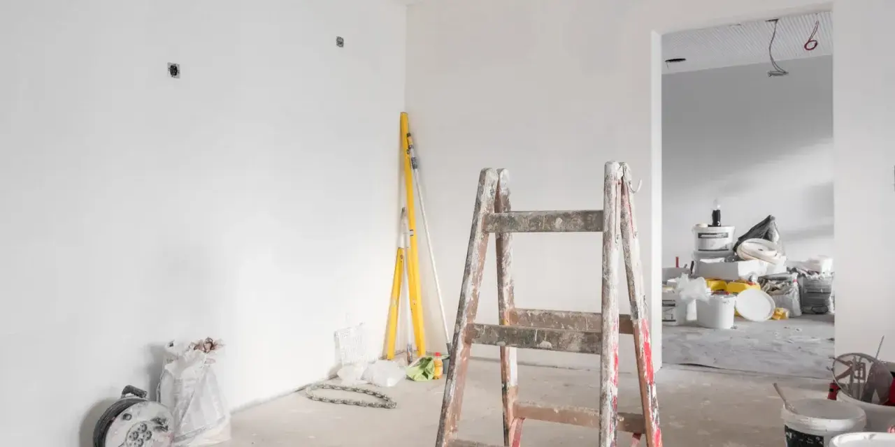 Remont starego domu w toku. Drewniana drabina, poziomice i materiały budowlane czekają na dalsze prace.